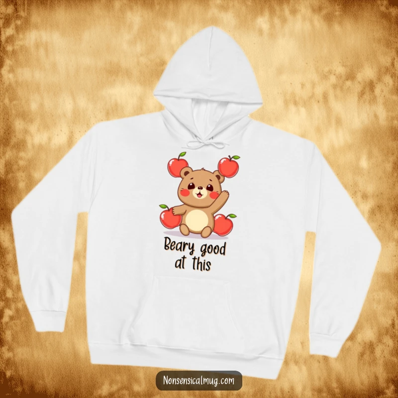 Funny hoodie design featuring a round, jovial bear character in the act of juggling three shiny apples, looking endearingly awkward.